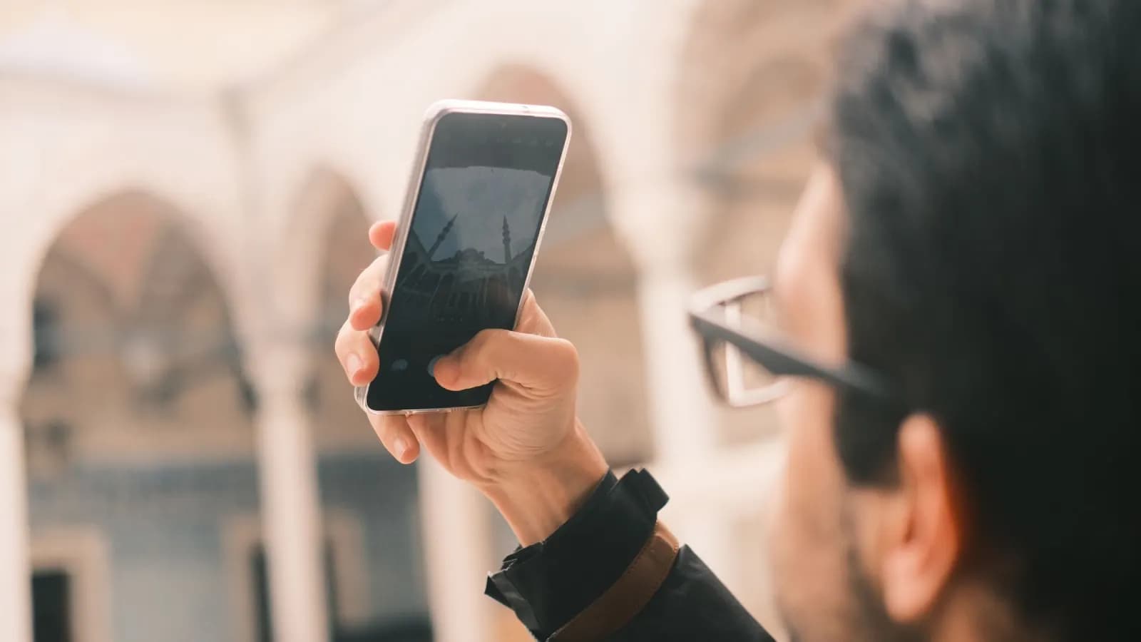 Traveler using a phone outside a mosque before an Umrah journey