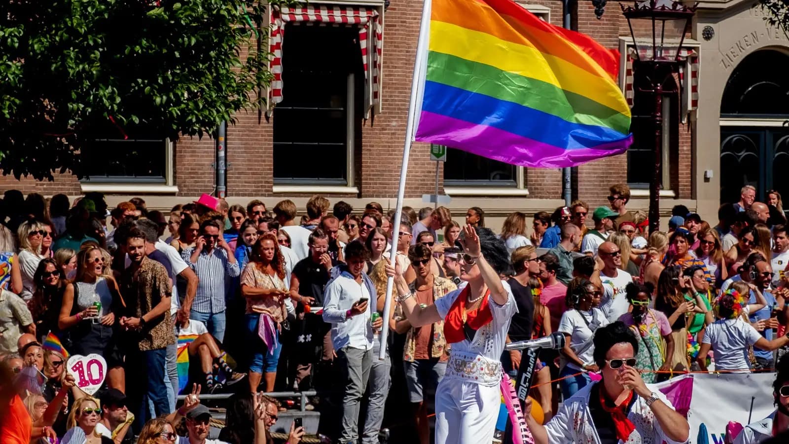 Canal Parade boat and crowd beneath a rainbow flag in Amsterdam